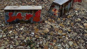 Una playa rocosa con objetos metálicos oxidados y vista al mar bajo un cielo nublado.