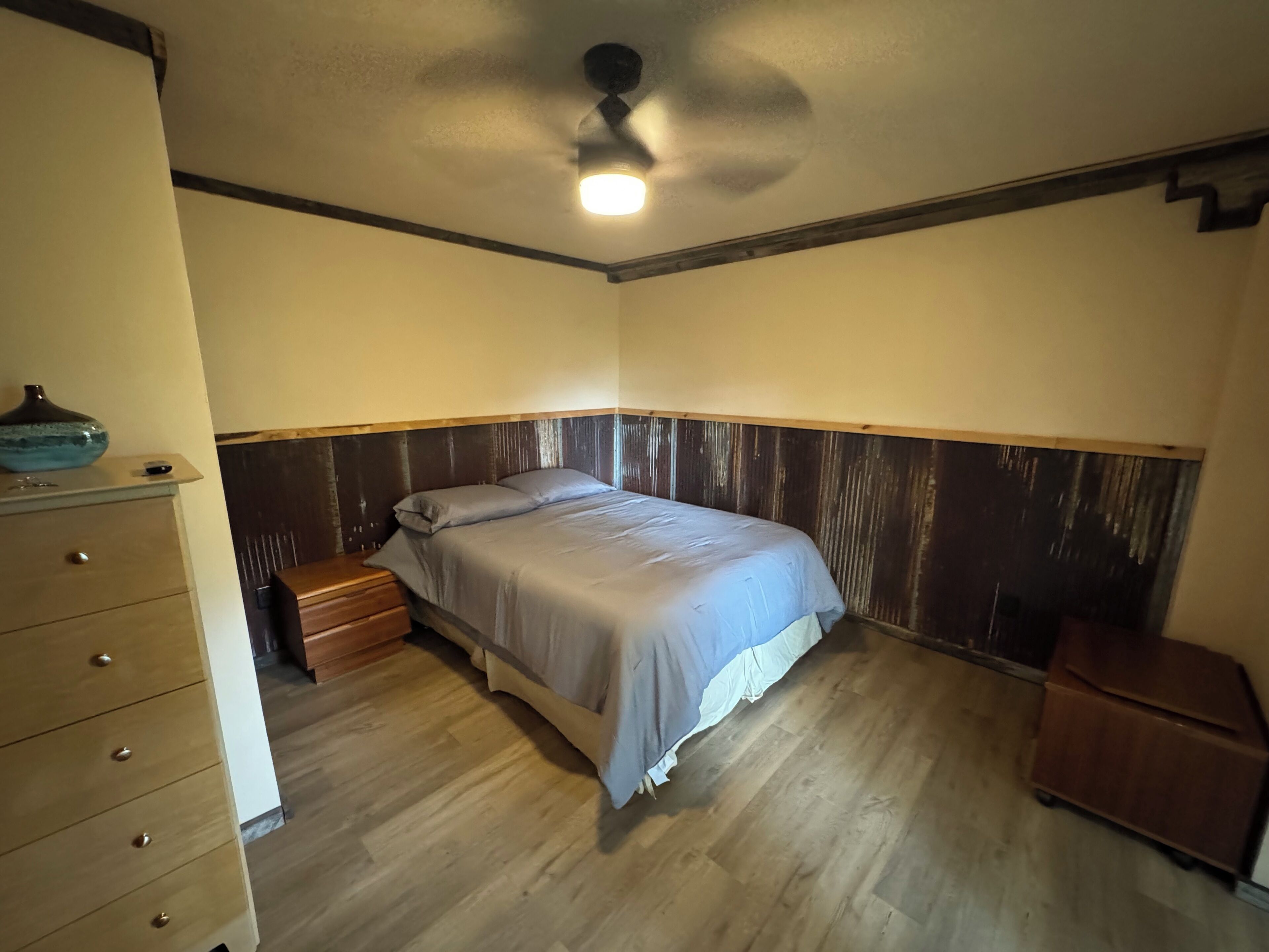 A bedroom with a bed, wooden dresser, nightstand, and a ceiling fan.
