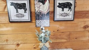 Et træinteriør med et bord, hvorpå der står en vase med tørrede blomster, samt billeder af oksekød, kylling og svinekød på væggen.