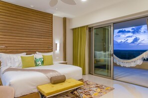 A hotel room with a large bed, a small bench, a view of the ocean through a sliding glass door, and a balcony with a hammock. - Oceanfront Paradise: Stunning 2-Bedroom Suite in Luxurious 5 Star Resort (Cancún)
