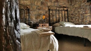 A bedroom with two beds, a stone wall, a chandelier, and a suitcase on the nightstand. - Country House 'La Casa Del Chileno' with Sea View, Private Terrace and Private Garden (Lierganes)