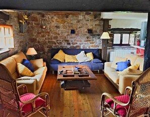 Un salon chaleureux avec un mur en pierre, deux canapés, une table basse, des fauteuils en osier et une lampe.