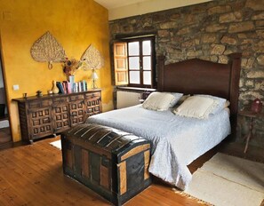 Une chambre avec un lit en bois, un mur en pierre, une commode en bois et un coffre ancien.