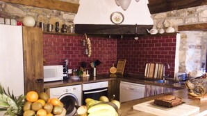 Une cuisine avec un mur en pierre, des poutres en bois, un mur de crédence en briques et divers appareils de cuisine.