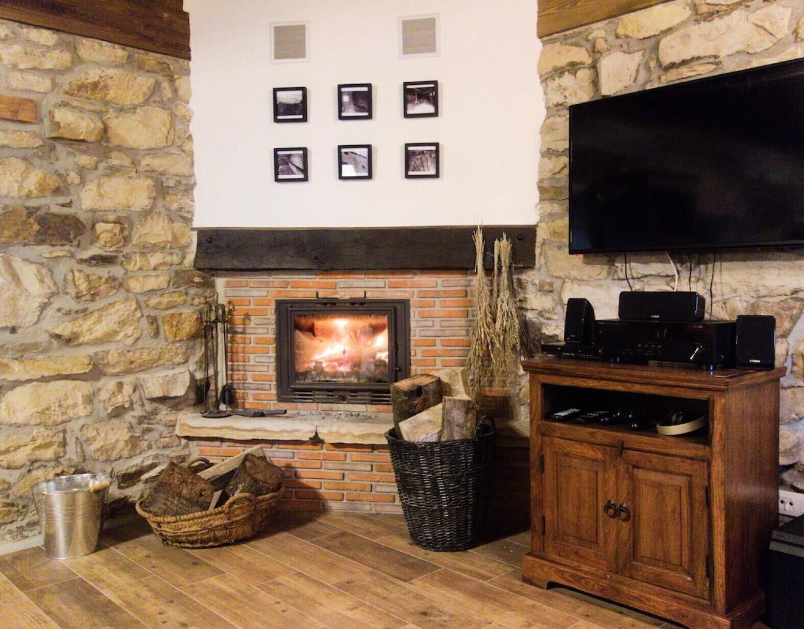 A stone wall, a fireplace with a fire, a television mounted on the wall, and a wooden cabinet.
