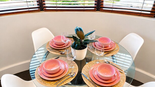 A round glass table with pink plates and silverware, surrounded by white chairs, in a room with a view through large windows. - Perfect sunny Studio in the city- Broadway- Chippendale (Chippendale)