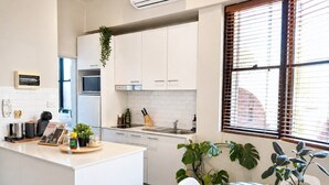 A modern kitchen with white cabinets, a central island, and a dining area with a glass table and chairs. - Perfect sunny Studio in the city- Broadway- Chippendale (Chippendale)