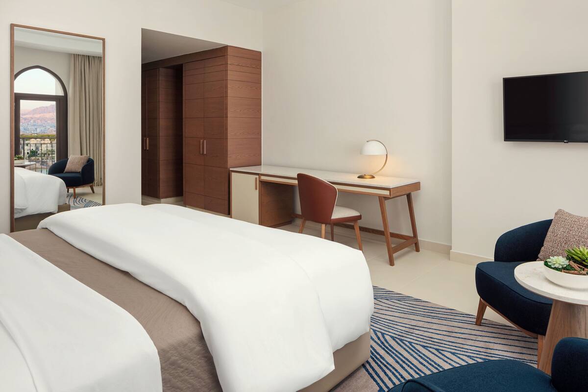 Una habitación de hotel con cama, escritorio, silla, televisor y vistas de la ciudad.