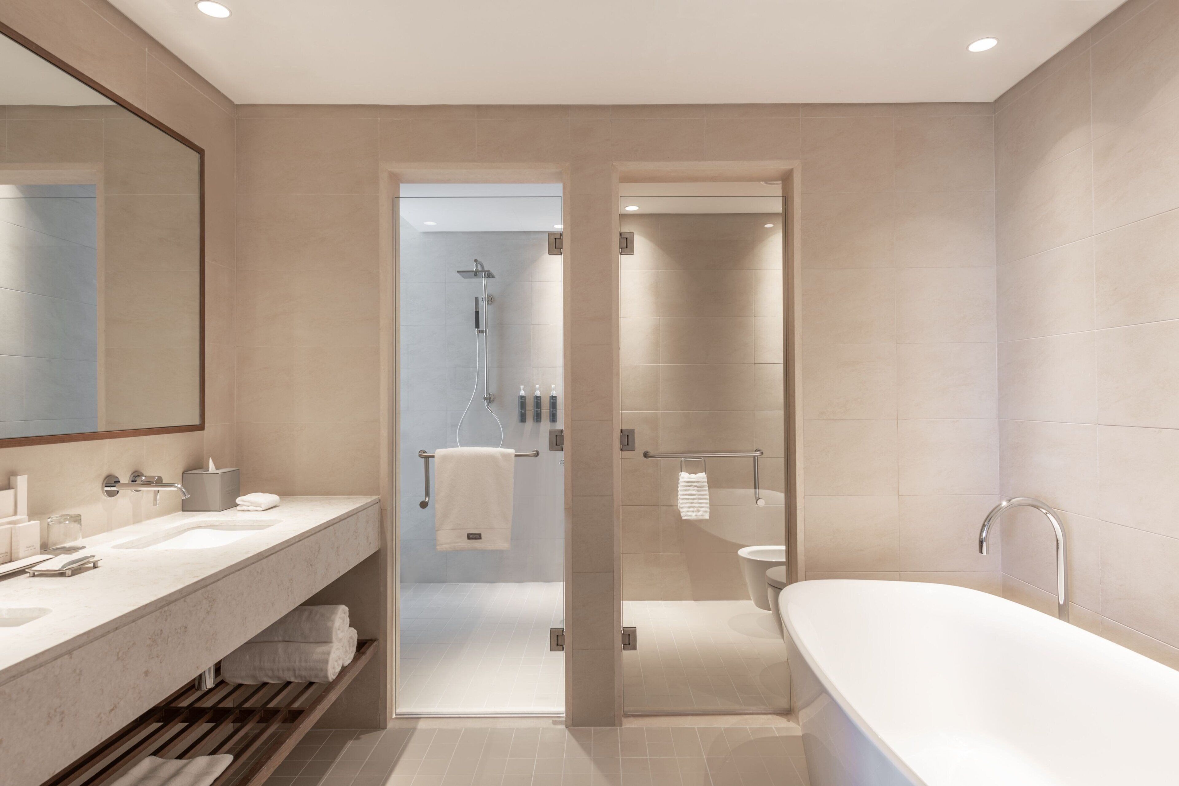 Un baño moderno con una bañera grande, una ducha con cerramiento de vidrio y un tocador con espejo y varios lavamanos.