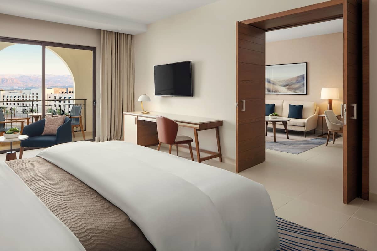 Habitación de hotel con una cama grande, un escritorio, un televisor y un balcón con vistas a la ciudad.