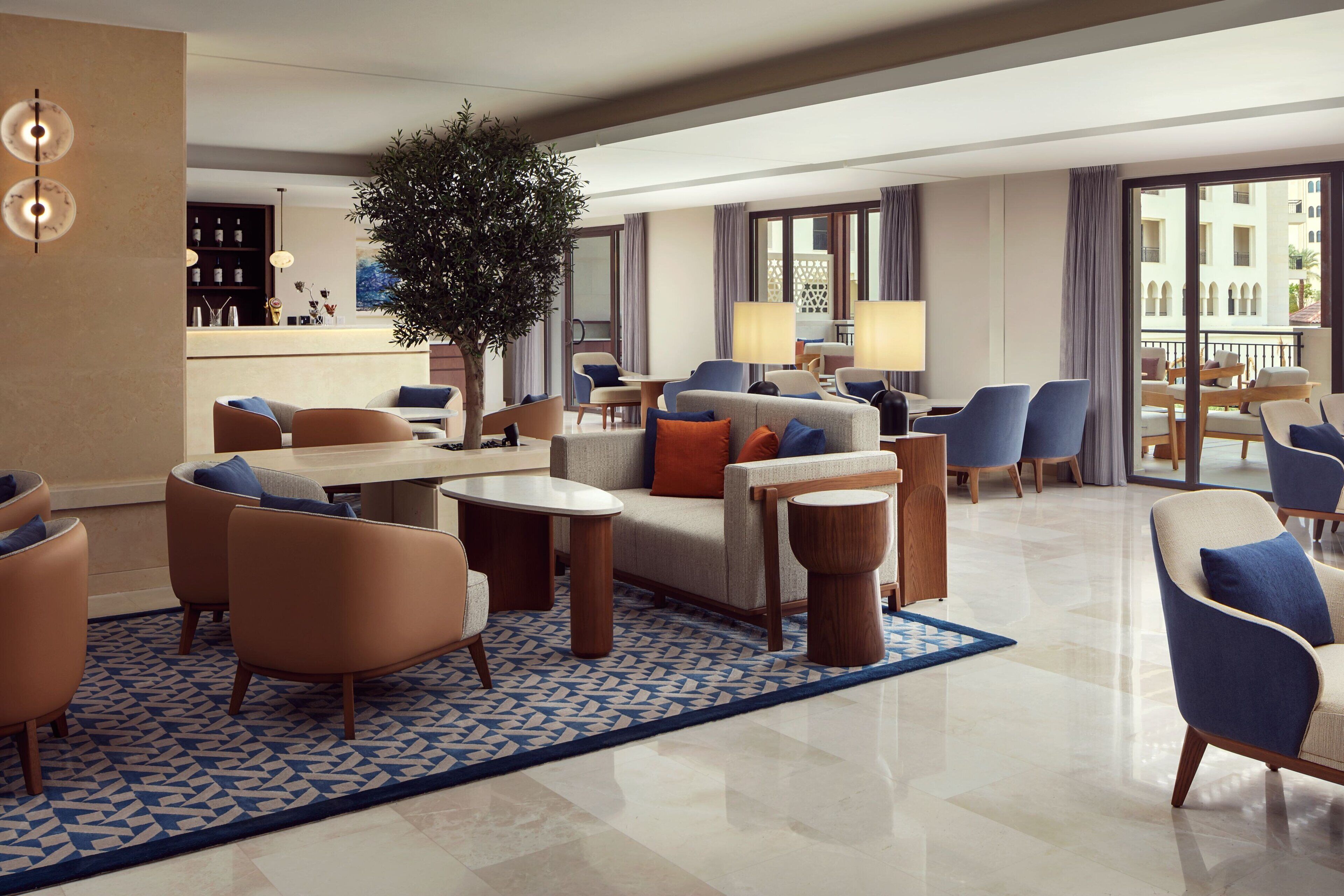 Een ruime hotellobby met een centraal zithoek, een bar en een groot raam met uitzicht op de skyline.
