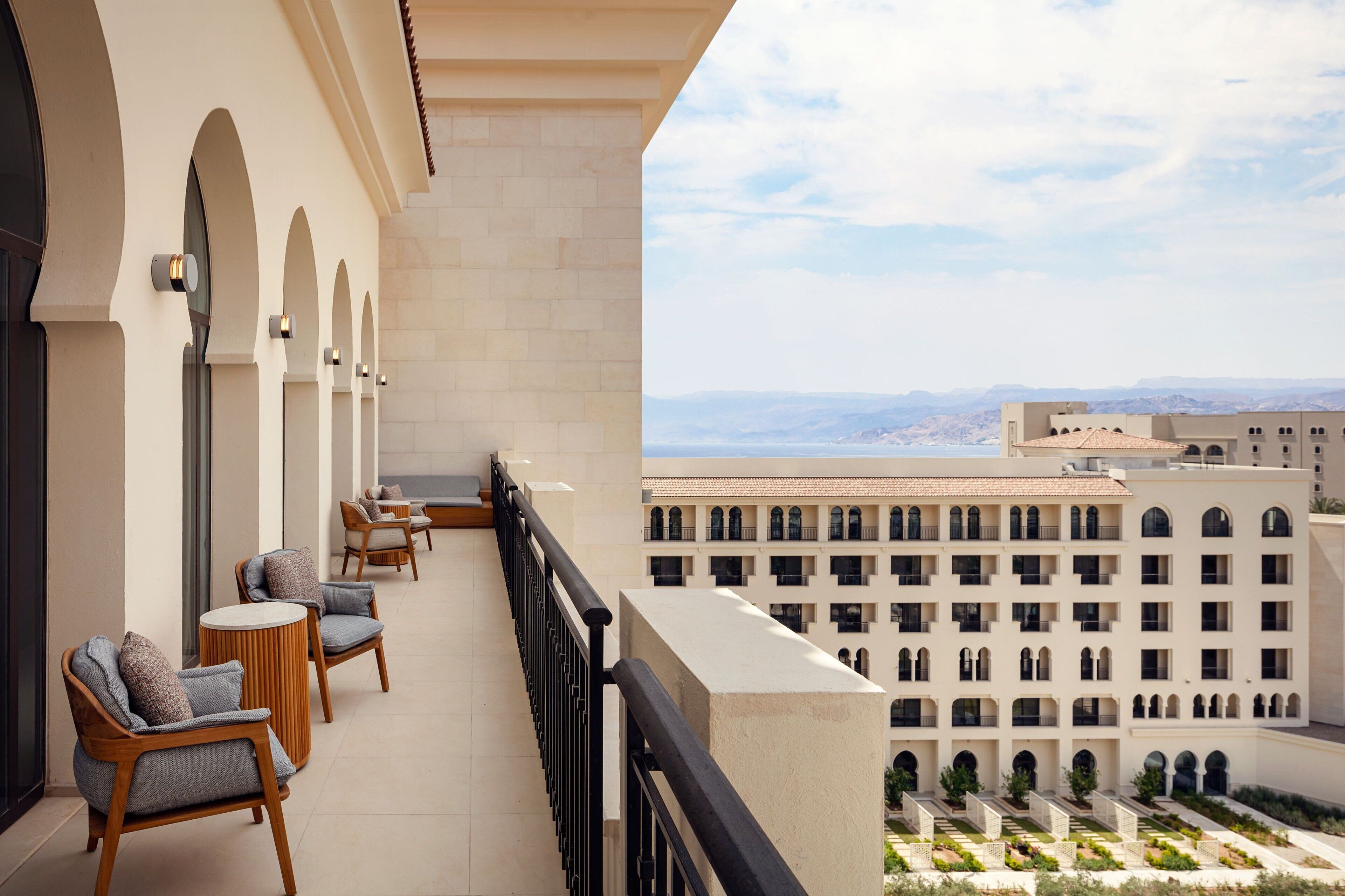 A balcony with seating, a view of a building with multiple windows, and a clear sky.