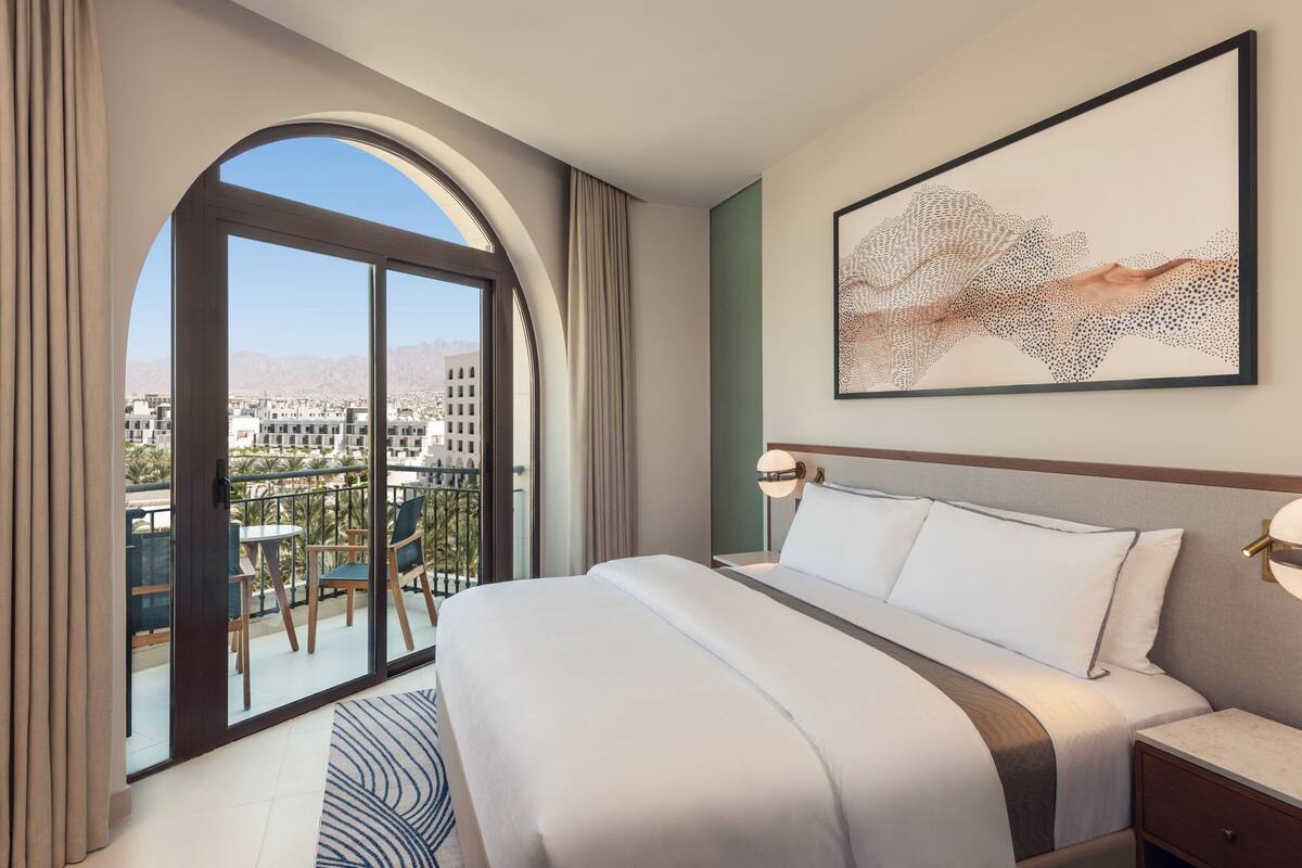 Habitación de hotel con una cama grande, un balcón que ofrece vistas a la ciudad y una obra de arte moderno en la pared.