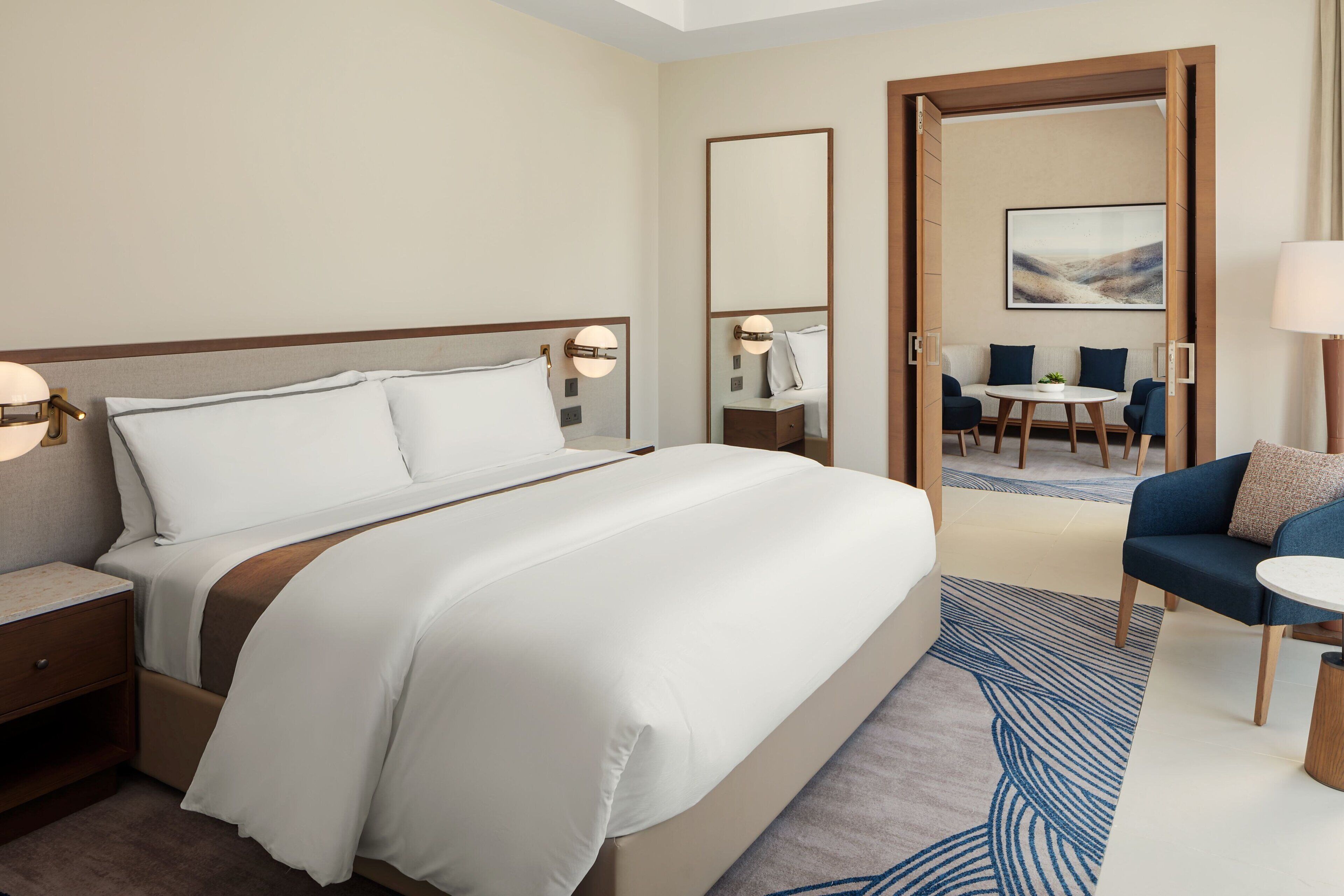 Habitación de hotel con una cama grande, mesitas de noche, un escritorio, una silla y vistas al área de recepción.
