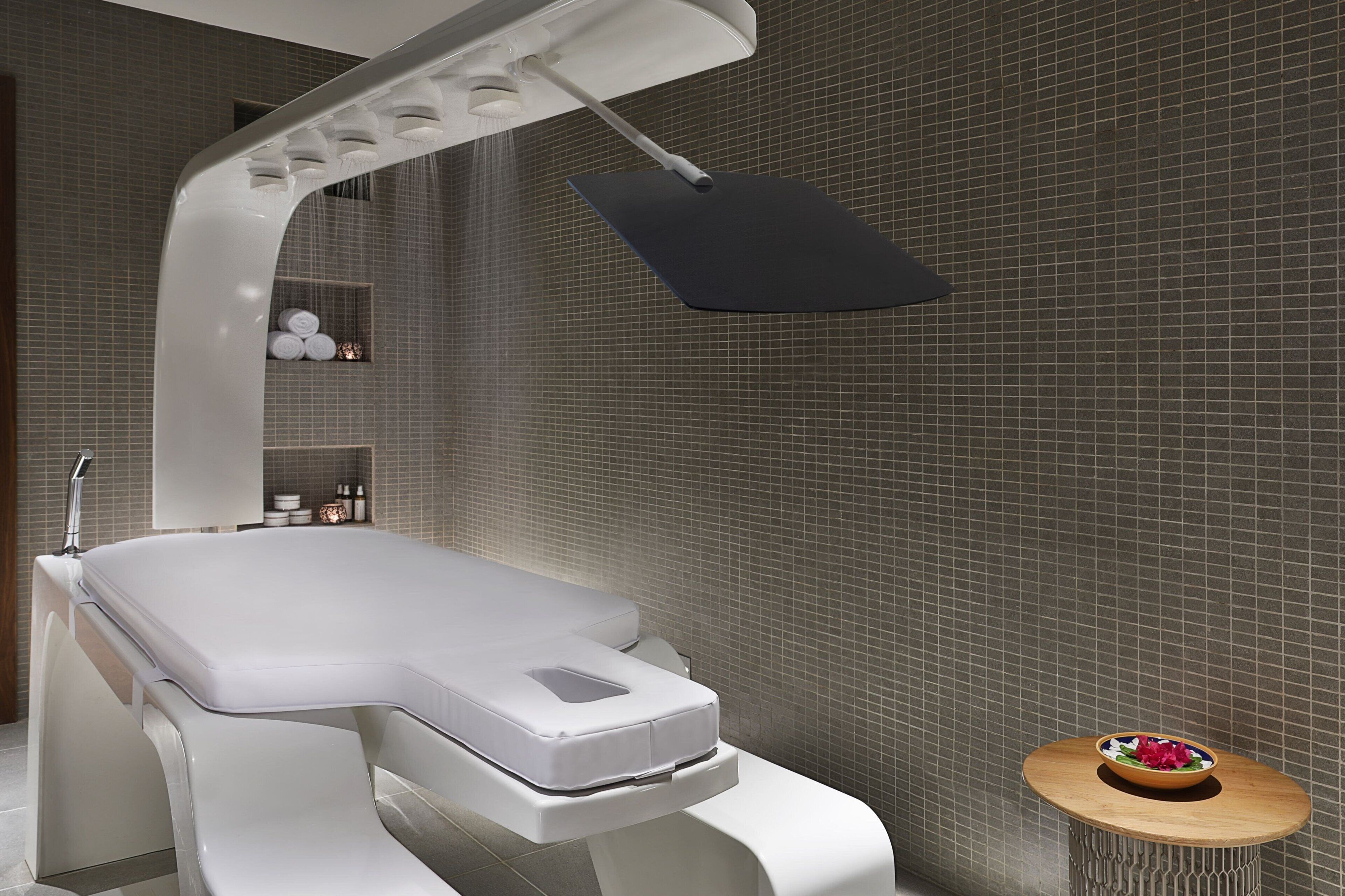 Un baño moderno con una bañera blanca, un cabezal de ducha y una pequeña mesa de madera con un frutero.