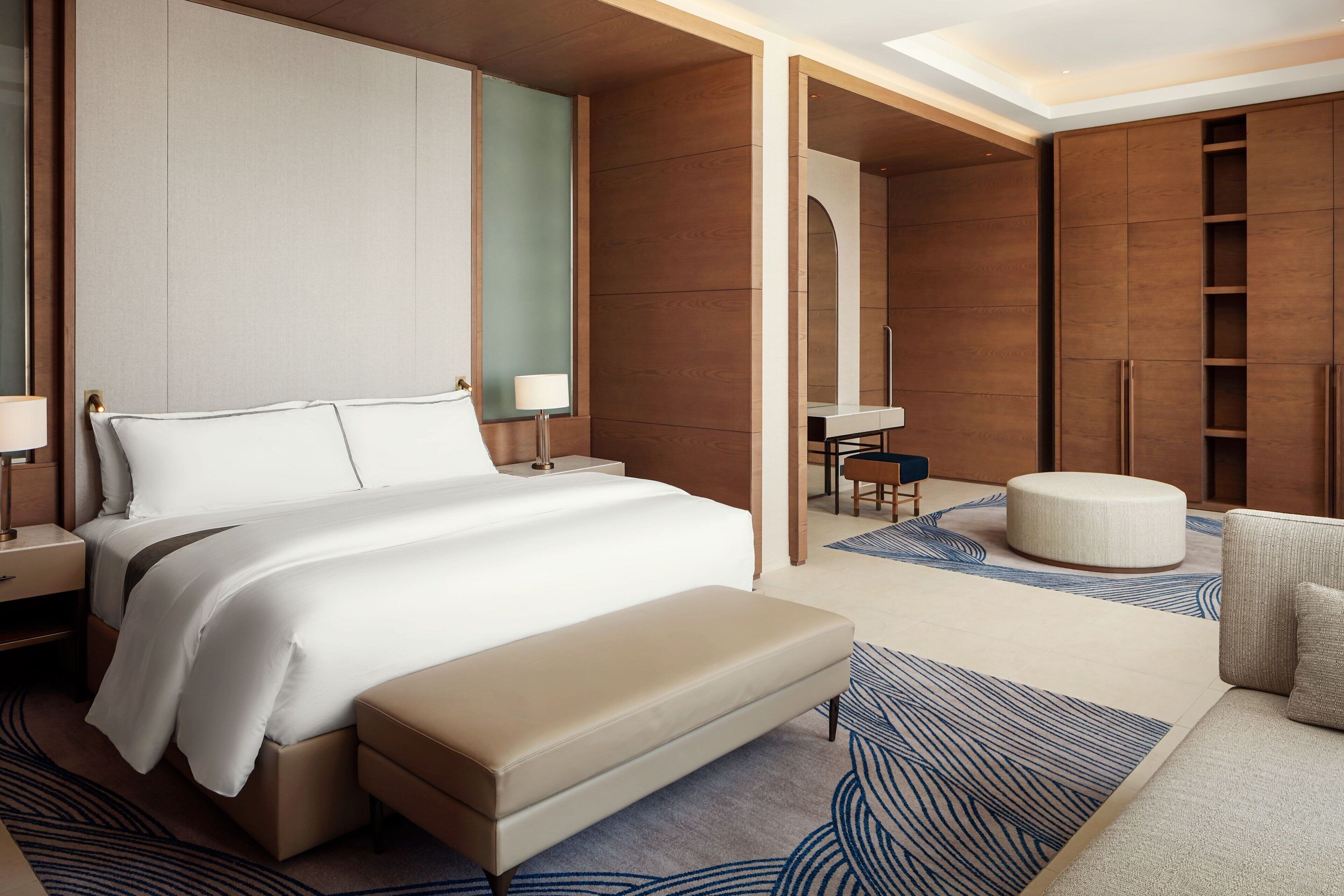 A modern hotel room with a large bed, a bench, a desk, and a wardrobe.
