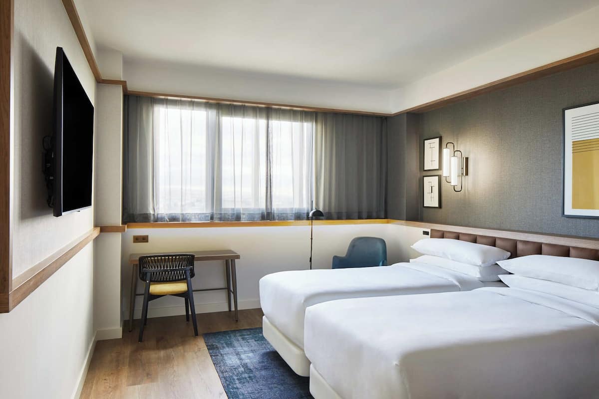 A hotel room with two beds, a desk, a chair, a TV, and a window with curtains.