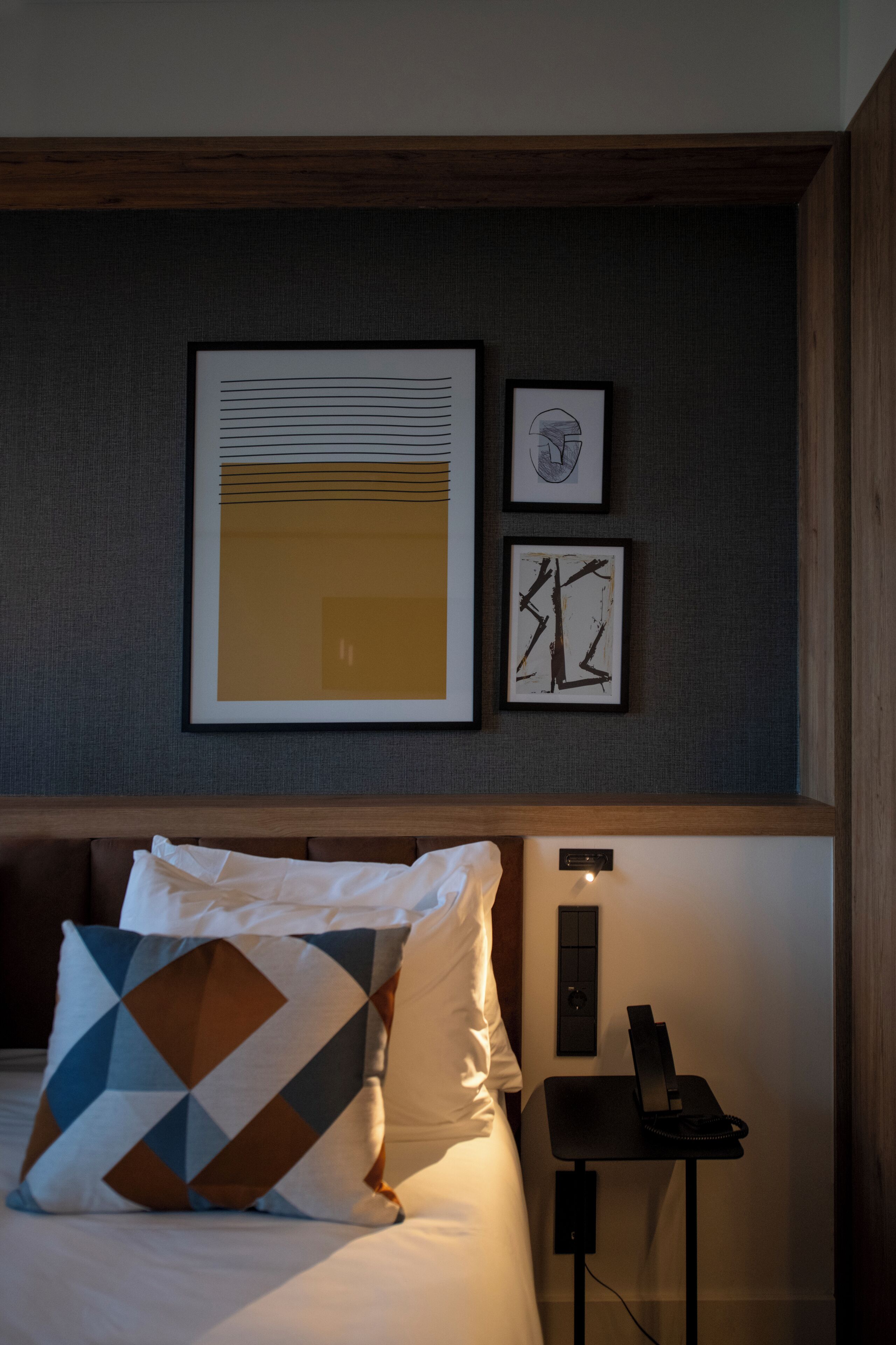 Habitación de hotel con cama, almohadas, mesita de noche con teléfono y cuadros en la pared.