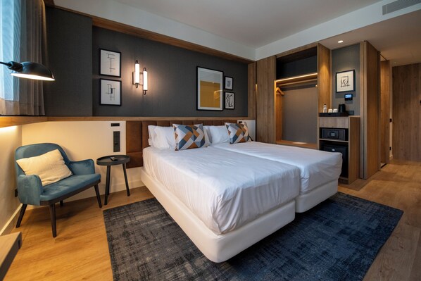 A modern hotel room with a large bed, a seating area with a chair, a small table, and a wardrobe. - Four Points by Sheraton Barcelona Airport (Viladecans)