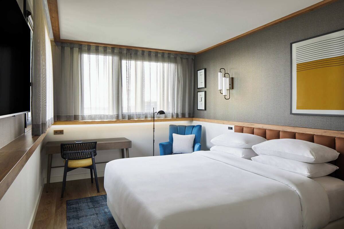 A hotel room with a large bed, a desk, a chair, and a window with curtains.