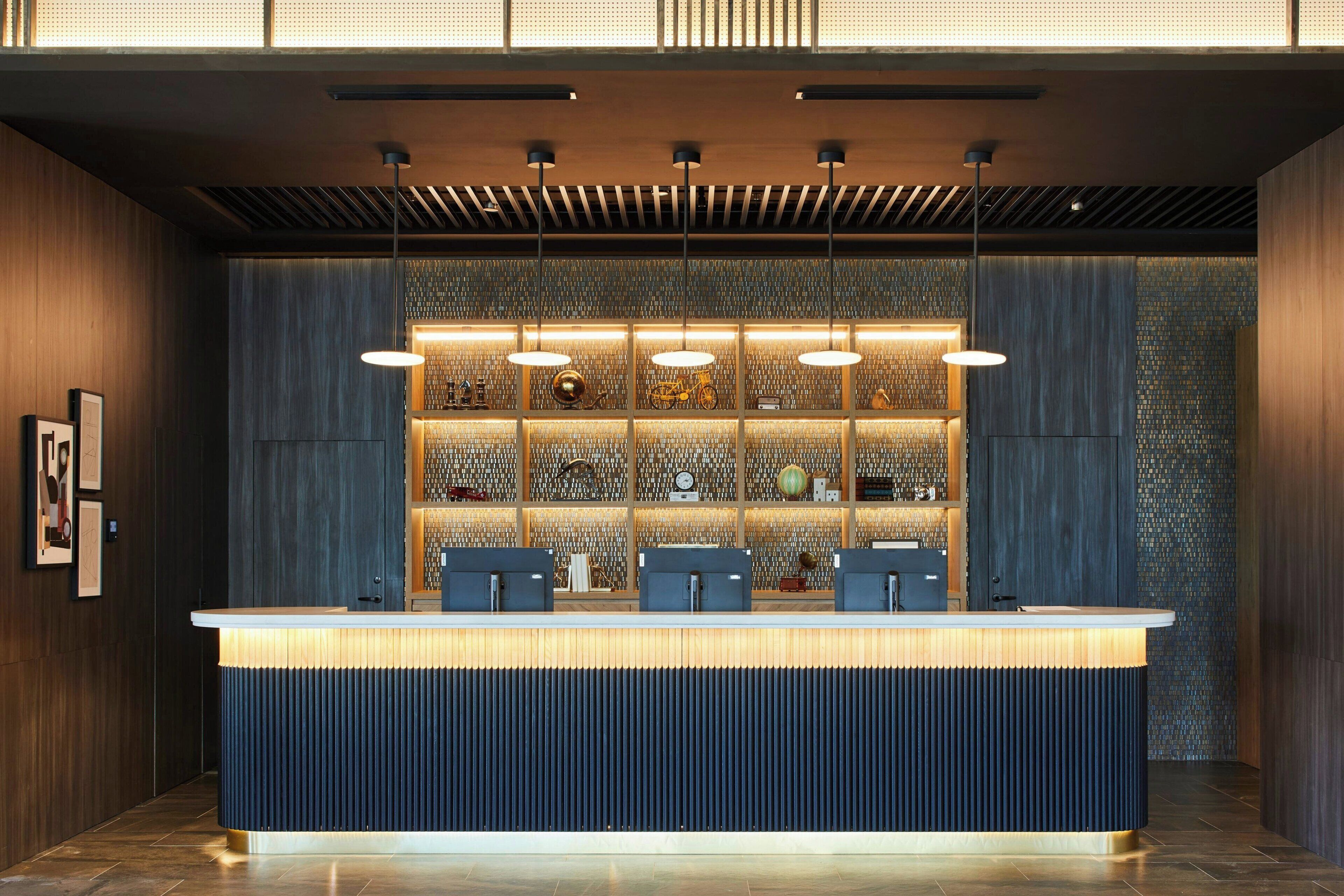 Un mostrador de recepción de diseño moderno, con una combinación de colores azul y madera oscura, y una pared decorativa con varios objetos e iluminación.