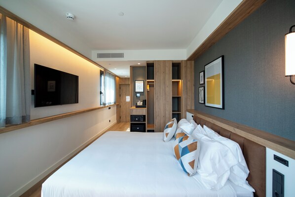 A hotel room with a large bed, a flat-screen TV mounted on the wall, built-in shelving, and a bedside table. - Four Points by Sheraton Barcelona Airport (Viladecans)