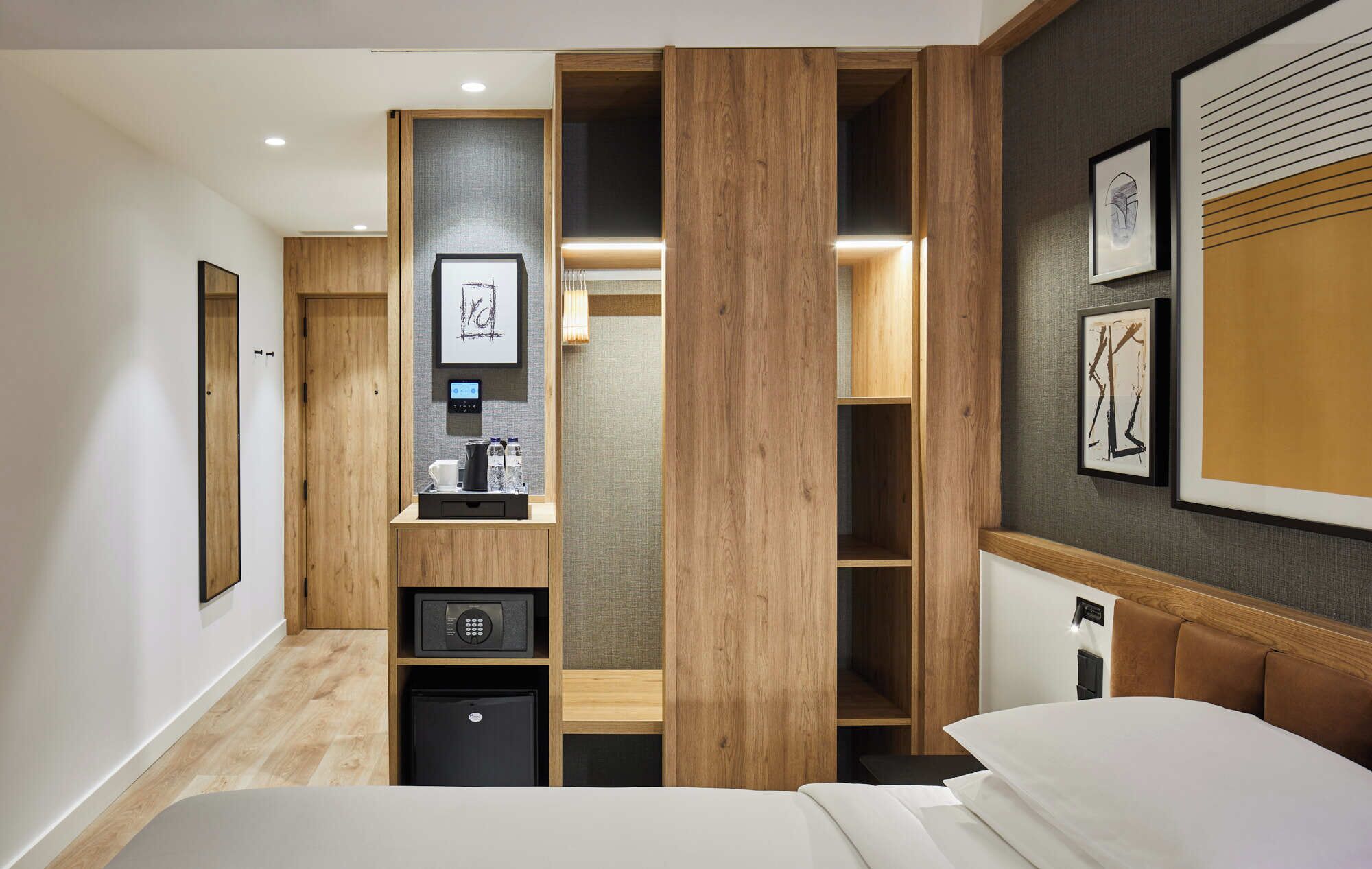 A hotel room with a bed, a desk with a coffee maker, a mini-fridge, a safe, and a large mirror.