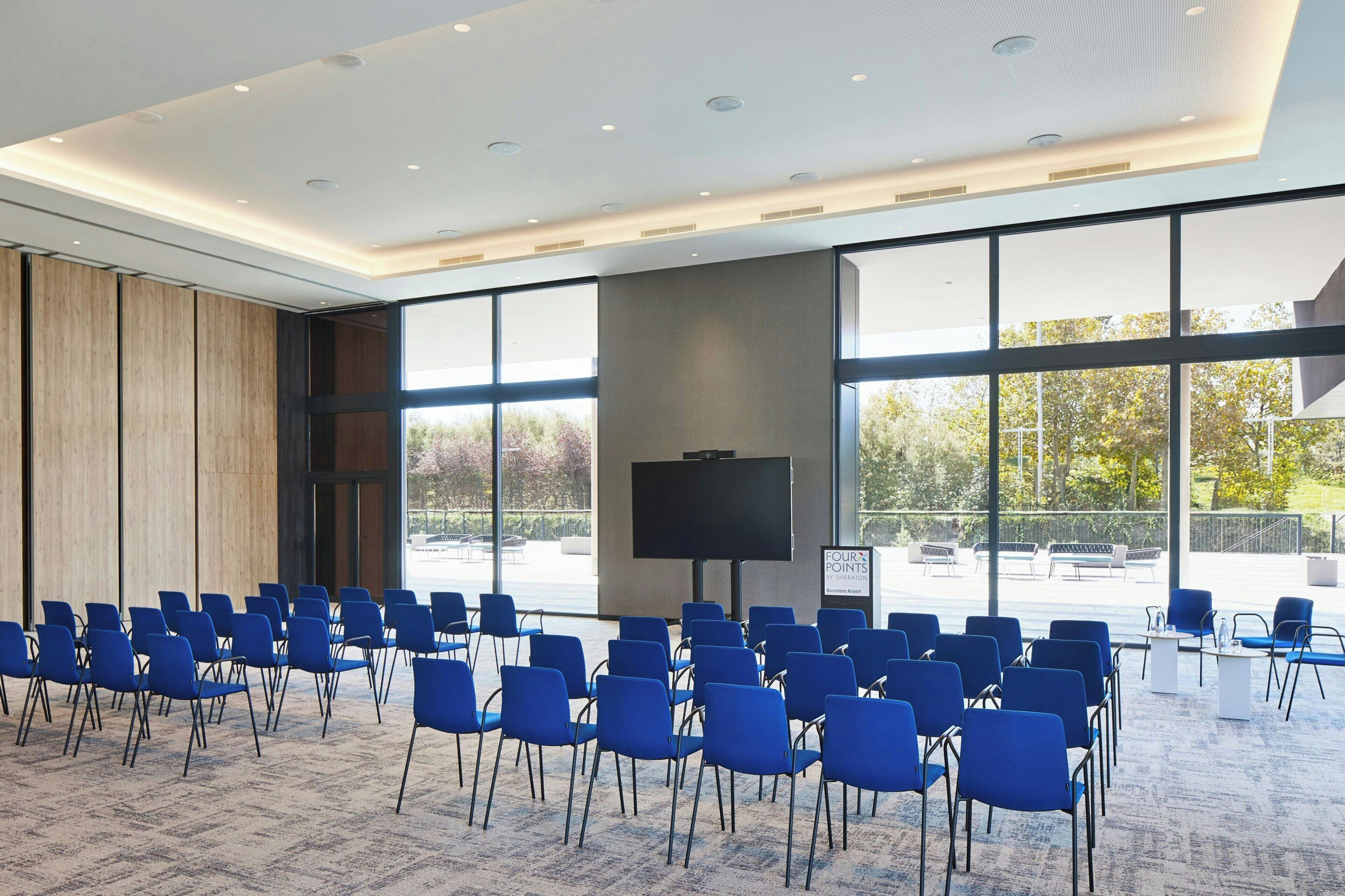 A conference room with rows of blue chairs, a large screen, and a view of the outdoors.