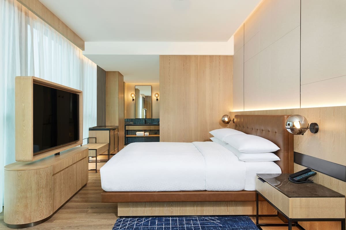 Une chambre d’hôtel moderne avec un grand lit, une télévision, une table de chevet et une salle de bain visible au fond.