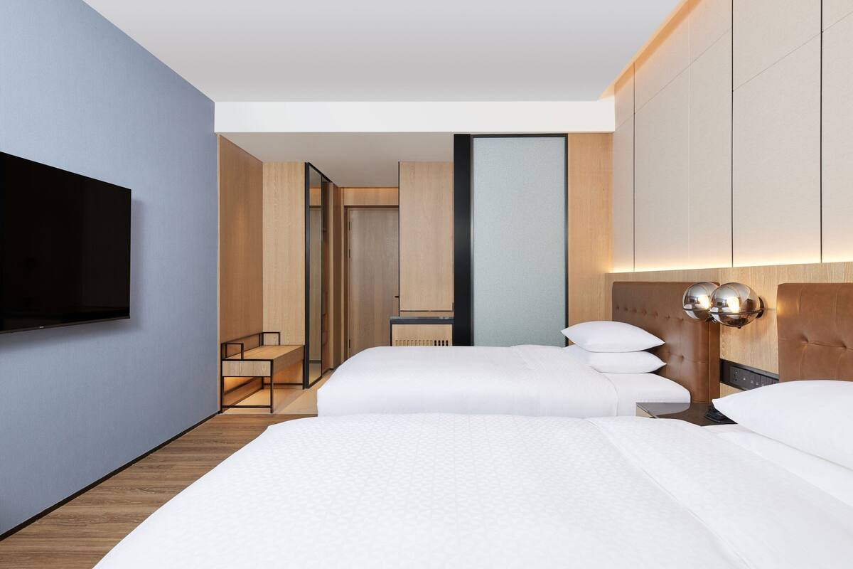 Une chambre d’hôtel moderne avec un grand lit, un téléviseur fixé au mur et une tête de lit en bois.