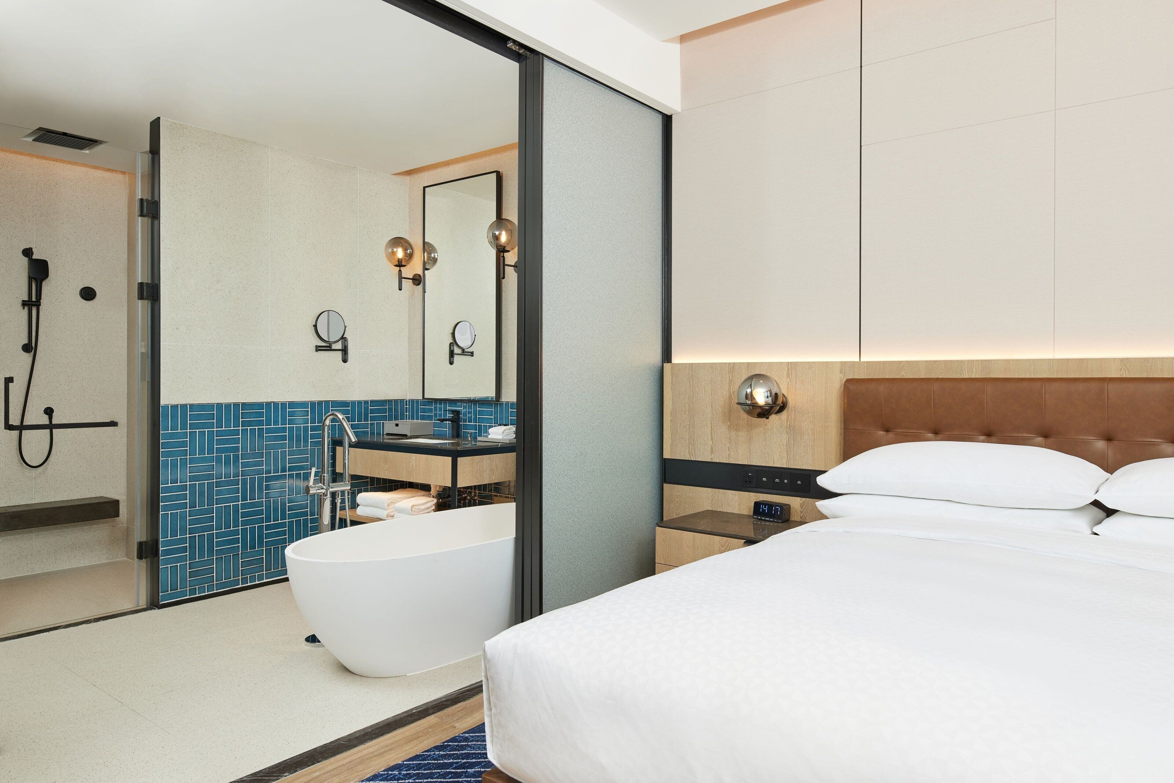 A modern hotel room with a large bed, a separate bathroom with a bathtub, and a shower.