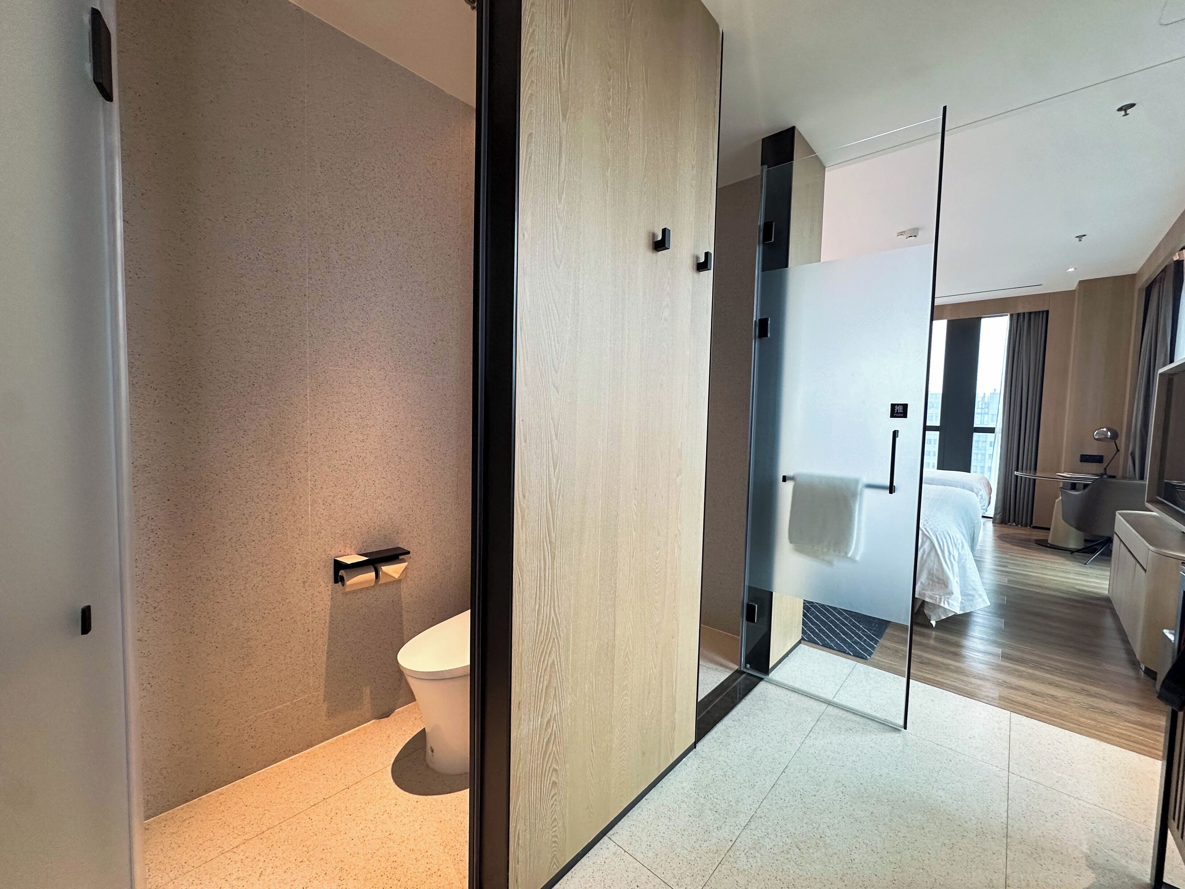 Ein modernes Hotelzimmer mit einem großen Spiegel, einem Bett, einem Schreibtisch und Blick auf die Stadt.