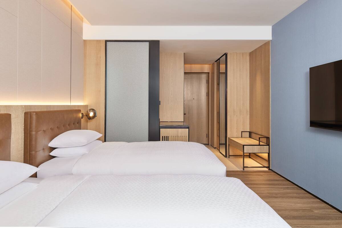 Une chambre d’hôtel moderne, dotée d’un grand lit, d’un bureau et d’un téléviseur fixé au mur.