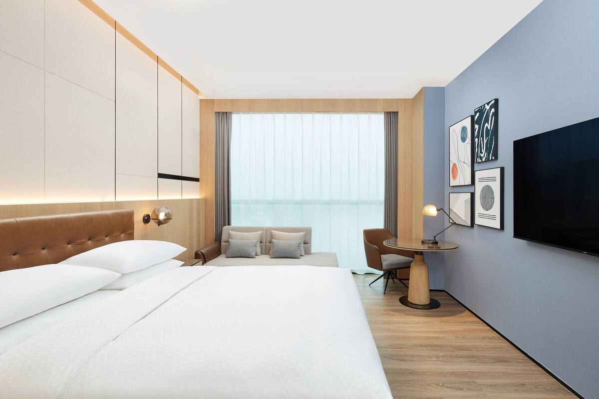 Une chambre d’hôtel moderne dotée d’un grand lit, d’un bureau avec une chaise, d’une télévision à écran plat et d’œuvres d’art accrochées au mur.