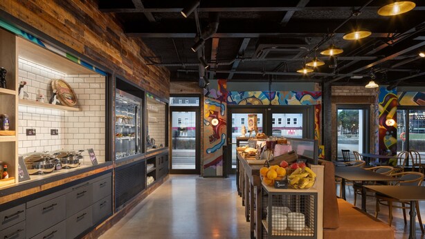 Un interior de restaurante moderno con una pared de acento de madera, un mostrador con productos alimenticios y una zona de comedor con mesas y sillas.