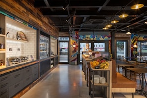 Un interior de restaurante moderno con una pared de acento de madera, un mostrador con productos alimenticios y una zona de comedor con mesas y sillas.