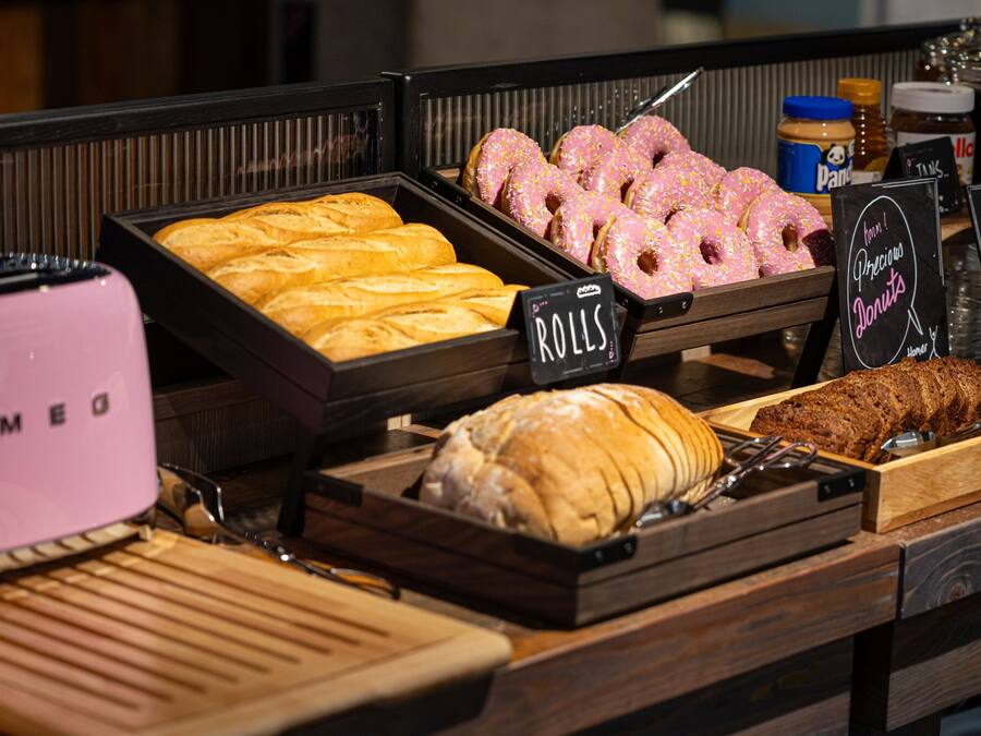 Una vitrina de panadería con diversas opciones de productos horneados, incluyendo bollos, rosquillas y una hogaza de pan.