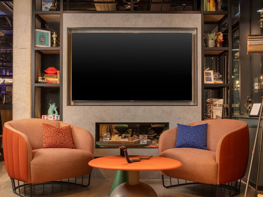 Una sala de estar moderna con dos sillones naranja, una mesa de centro redonda naranja y un televisor plano grande montado en la pared.