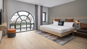 Una habitación de hotel moderna con una cama grande, vista al río y un balcón con barandilla.