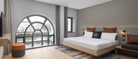 Una habitación de hotel moderna con una cama grande, vista al río y un balcón con barandilla.