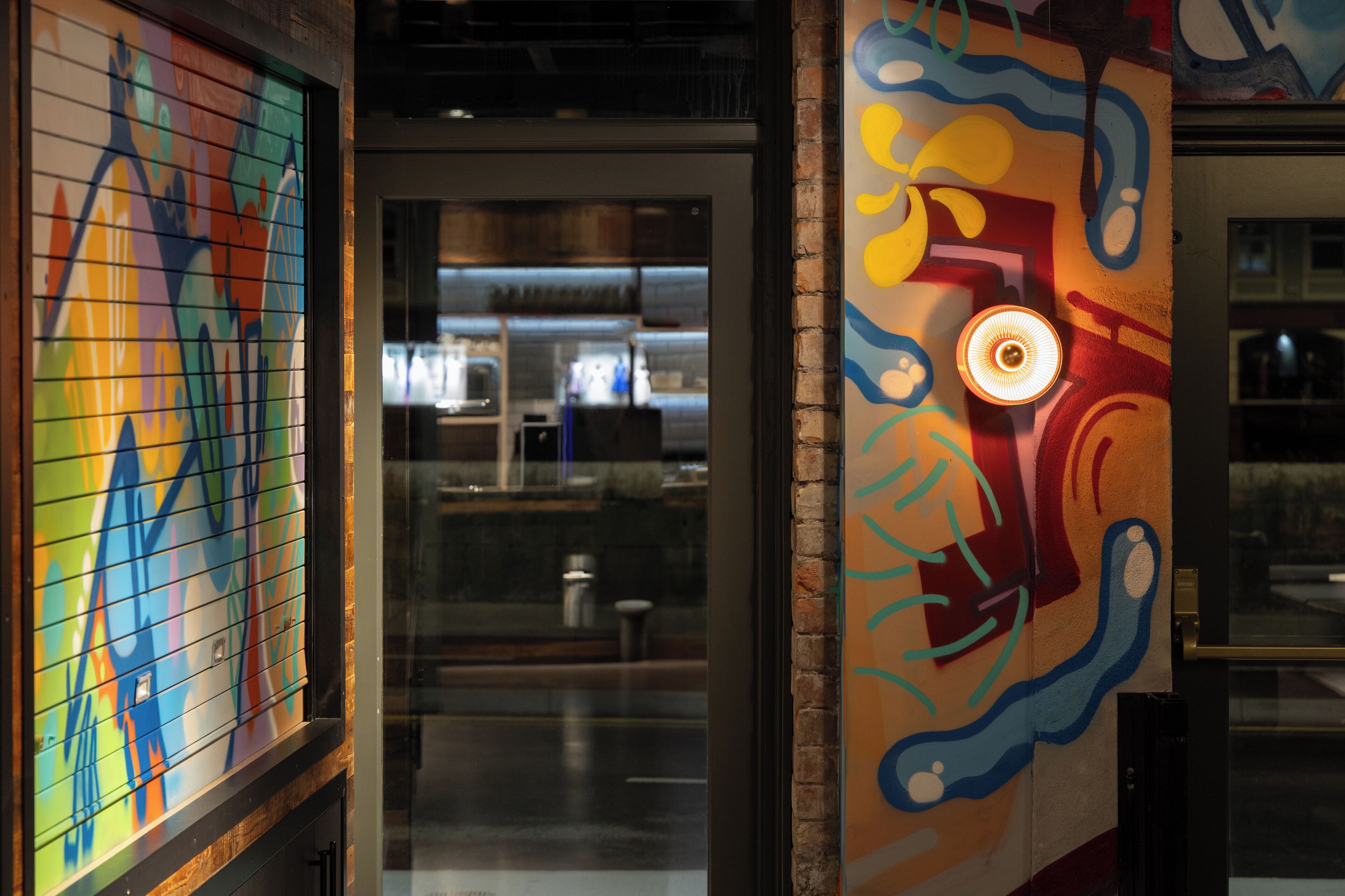 A colorful mural with abstract designs and a modern interior with a glass door leading to a kitchen area.