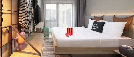 Une chambre d’hôtel moderne, dotée d’un lit, d’une table de chevet et offrant une vue sur la ville grâce à de grandes fenêtres.