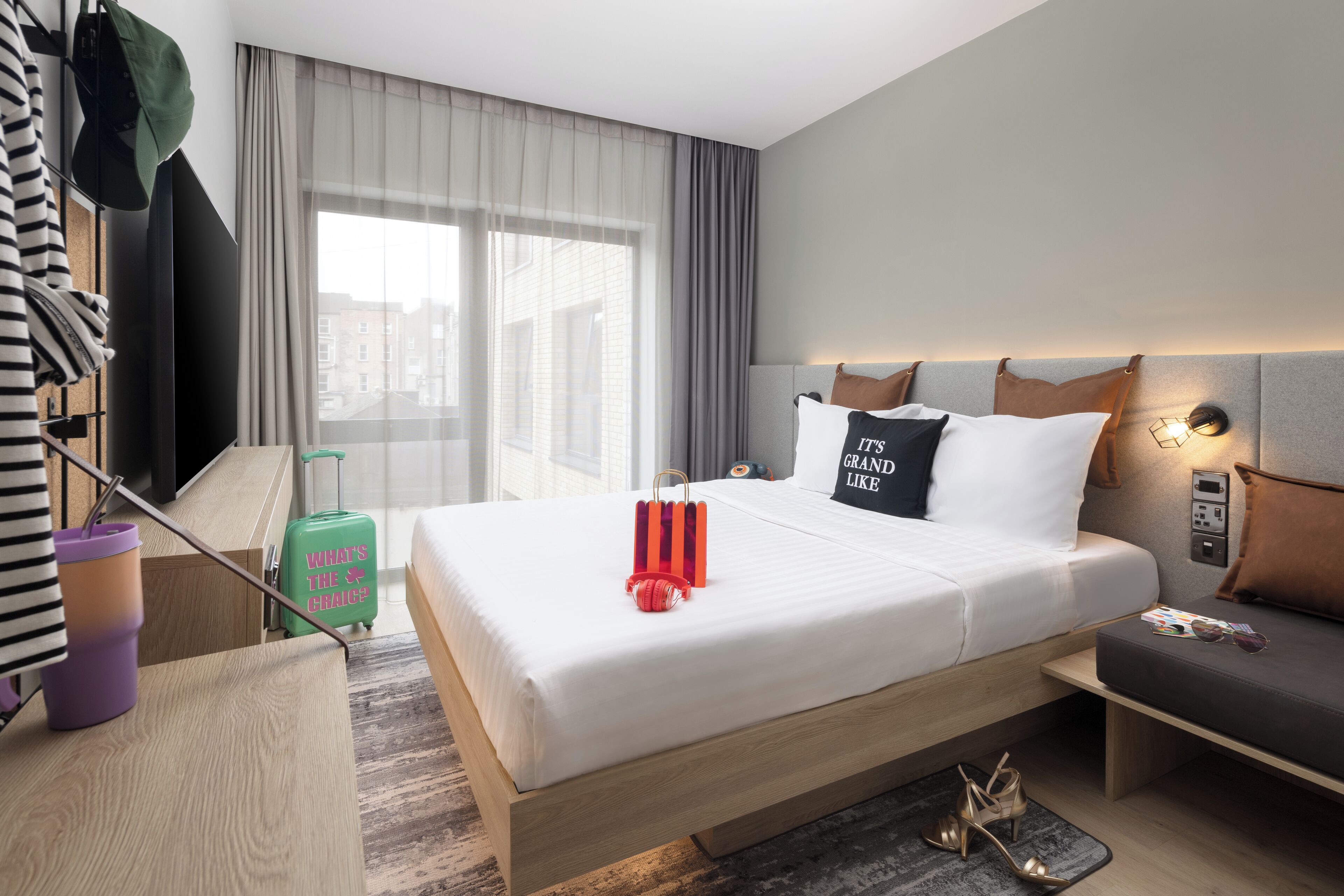 Una habitación de hotel con cama, escritorio, maleta y ventana con cortinas.