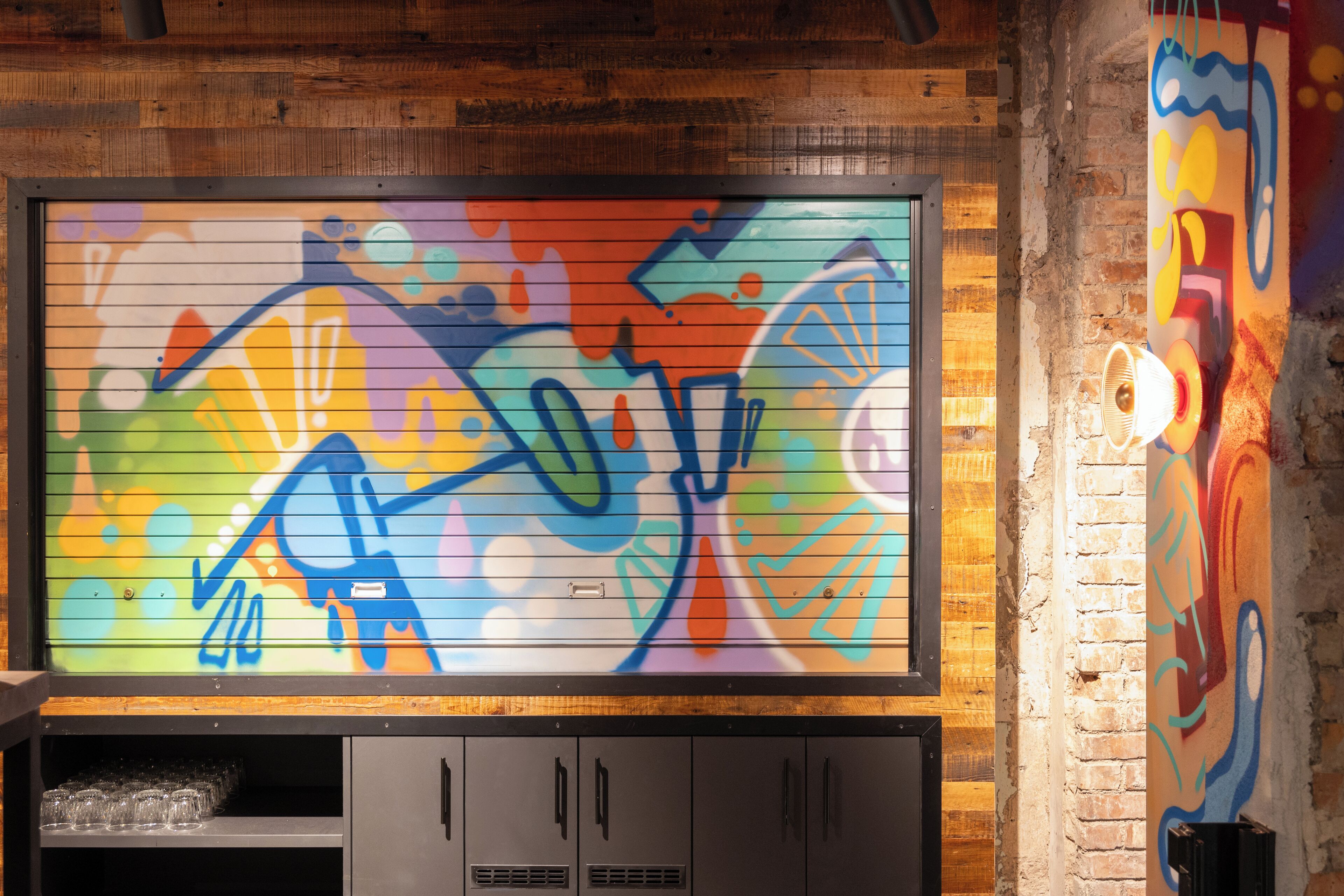 A colorful graffiti mural on a wall with a wooden ceiling and a metal-framed window.