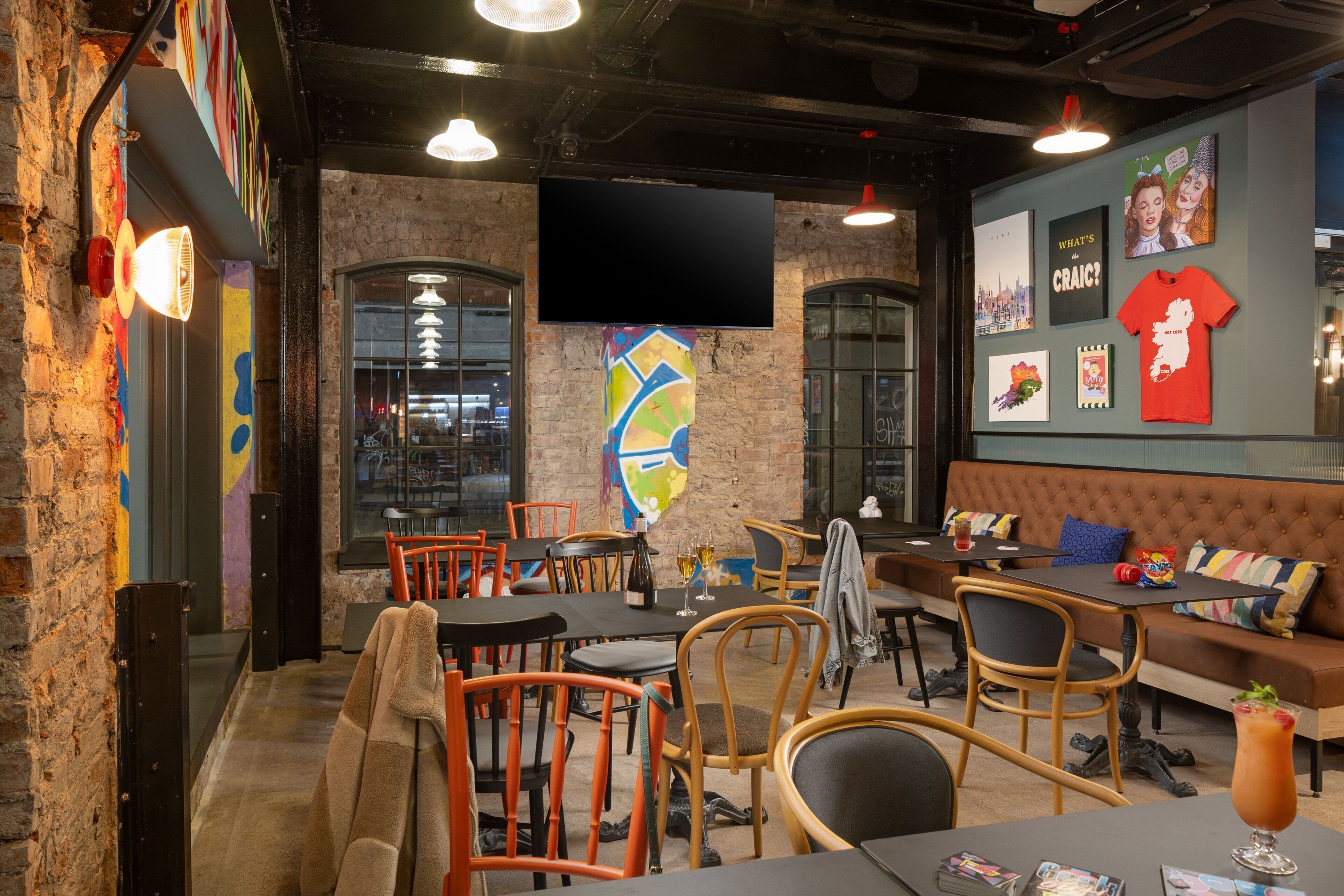 A cozy restaurant with brick walls, wooden chairs, and a large TV screen.
