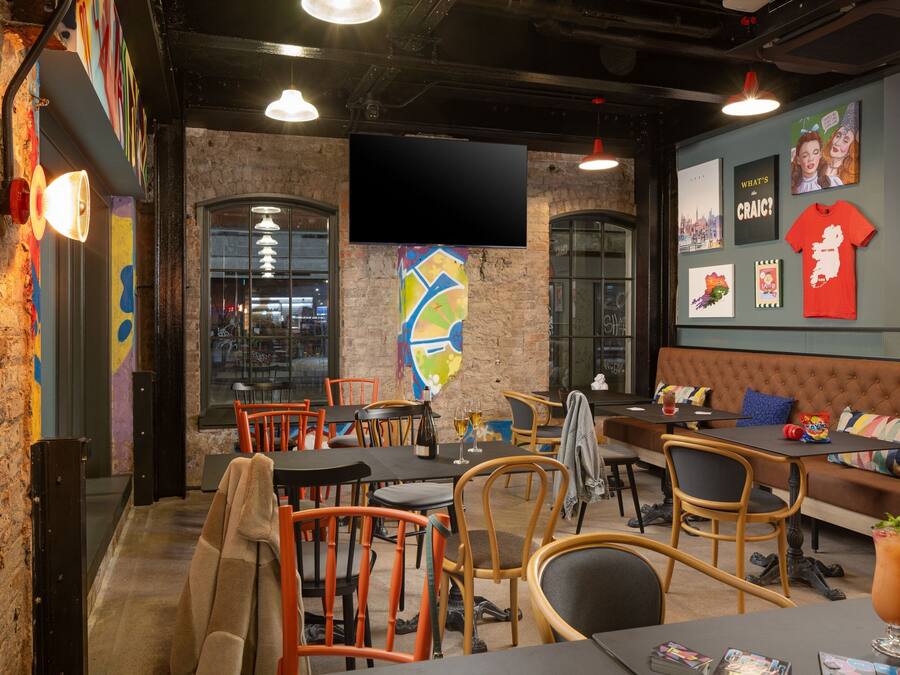A cozy restaurant with brick walls, wooden chairs, and a large TV screen.