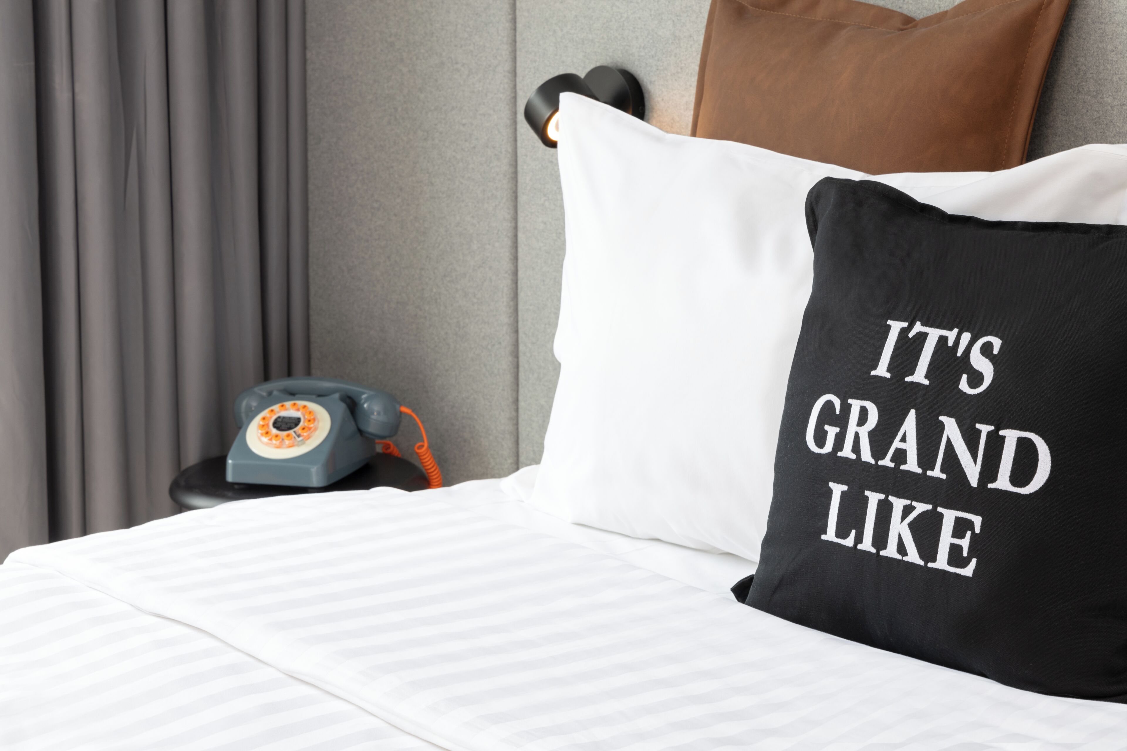 A bed with a white and black pillow, a telephone, and a brown pillow on a headboard.