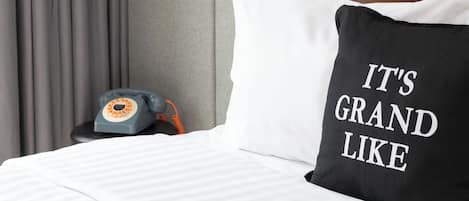 A bed with a white and black pillow, a telephone, and a brown pillow on a headboard.