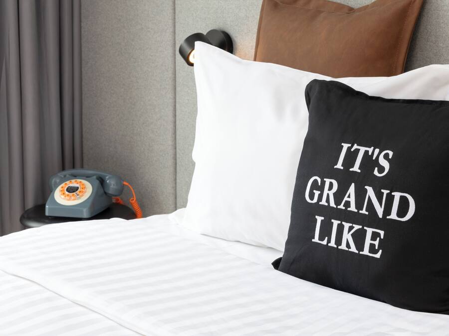 Una cama con almohada blanca y negra, un teléfono y una almohada marrón en el cabecero.