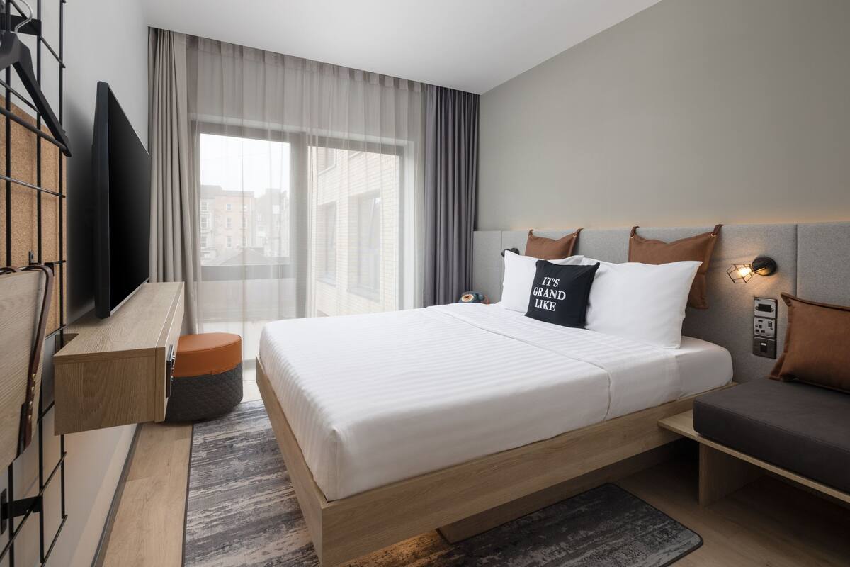A modern hotel room with a large bed, a TV, a desk, and a sofa.